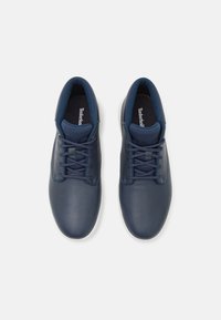 Um par de sapatos de couro azul-marinho com atacadores, colarinhos almofadados e solas brancas, vistos de cima sobre um fundo branco.