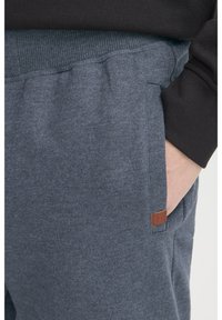 Grå fleece joggers med ribbet talje, sidelommer og et lille brunt læderlogo. Blød tekstur, afslappet pasform.