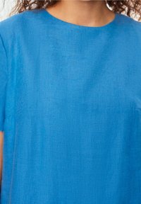 Top de lino azul con cuello redondo y mangas cortas, que presenta una textura suave y detalles de costura mínimos.