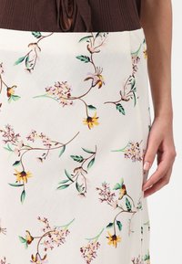 Blomstrete skjørt med kremfarget bakgrunn, prydet med fargerike blomster i rosa, gult og grønt på en jevn stoffstruktur.