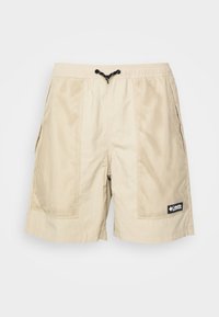 Shorts décontractés beiges avec panneaux latéraux en mesh, taille élastique, cordon de serrage noir, poches latérales et un patch logo Columbia sur la jambe droite.