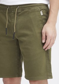 Gröna bomullsshorts med elastisk midja, dragsko, sidofickor och en liten logg på vänster sida.