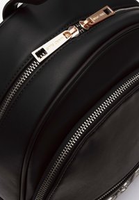 Sac à dos en cuir noir avec deux zips en argent et des accessoires en or rose. Texture lisse avec des bords arrondis et un design structuré.