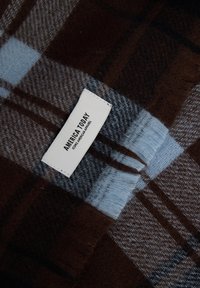 Braun-blau kariertes Halstuch mit weicher Textur; verfügt über ein weißes Etikett mit "AMERICA TODAY" in Schwarz aufgedruckt.