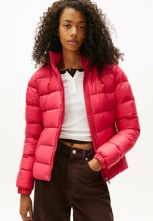Rode pufferjas met een doorgestikt ontwerp en een hoge kraag. Draag het over een witte top en bruine corduroy broek, wat een getailleerd silhouet laat zien.
