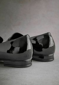 Black patent leather shoes with a sleek design, pointed toe, and low block heel. Smooth, shiny surface with subtle stitching details.