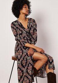 Czarna sukienka w wzór paisley, zapinana, z rękawami o długości trzech ćwiartek, z dekoltem w kształcie litery V oraz rozcięciem na udzie. Noszona z brązowymi zamszowymi botkami.