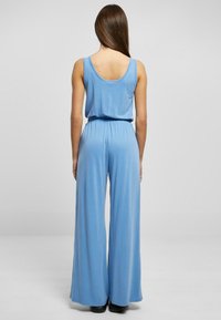 Blå ermeløs jumpsuit med løs passform, vide bukser og elastisk liv. Mykt stoff med glatt tekstur, minimalistisk design.