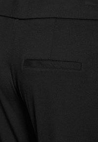 Pantalones de tela elástica negra con un bolsillo trasero que presenta un diseño de ribete horizontal. Detalles de costura visibles a lo largo de la cinturilla y los lados.