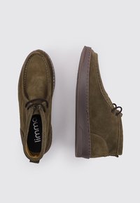 Un par de zapatos casuales de ante marrón con cordones marrones oscuros, un zapato visto desde arriba y el otro de perfil sobre un fondo claro.