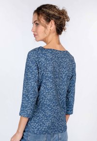 Bluse mit blauem Blumenmuster, dreiviertel Ärmel, weiter Ausschnitt, aus weichem Stoff. Rückansicht, die das detaillierte Blumendesign zeigt.