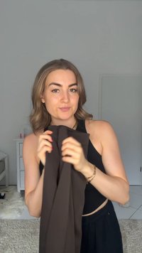 Leggings en tissu marron maintenus à mi-niveau, avec une texture lisse. Le modèle porte un débardeur noir, avec des murs de couleur claire en arrière-plan.