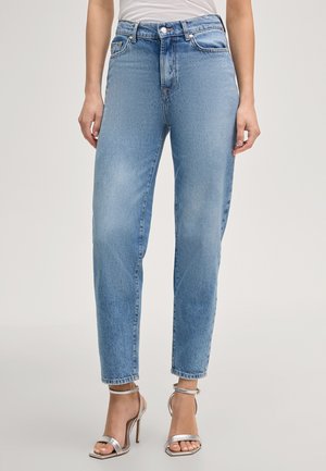 Frau trägt hoch taillierte, hellblaue Jeans mit geradem Bein, kombiniert mit silbernen hochhackigen Sandalen mit Knöchelriemen.