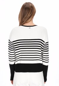 Pull en maille à rayures noires et blanches avec un bas uni noir. Il présente une texture côtelée, une coupe décontractée et un petit logo au dos.