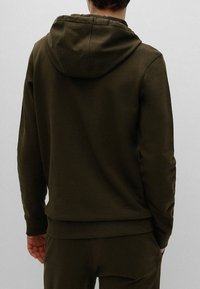 Olivově zelená mikina s kapucí z měkkého materiálu, vybavená klokáním kapsou, žebrovanými manžetami a lemem, zobrazená zezadu.