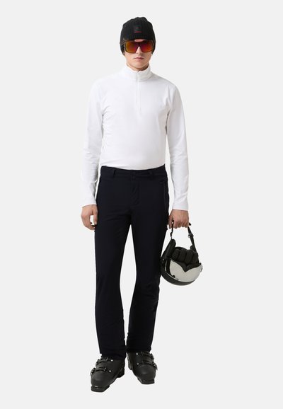 Bílý dlouhý rukáv, černá čepice, zabarvené sluneční brýle, námořnické kalhoty a černé lyžařské boty. Drží šedou a černou lyžařskou helmu.