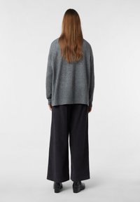 Helles graues, oversized Sweatshirt mit geripptem Saum, kombiniert mit weiten schwarzen Hosen und Stiefeletten, von hinten betrachtet. Glatte Textur.