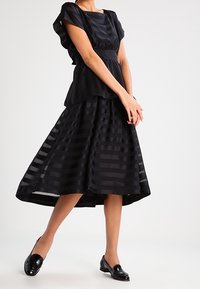 Sort stribet kjole med tætsiddende overdel og svajet skørt, der har en asymmetrisk kant og en subtil glans. Sættes sammen med sorte loafers.