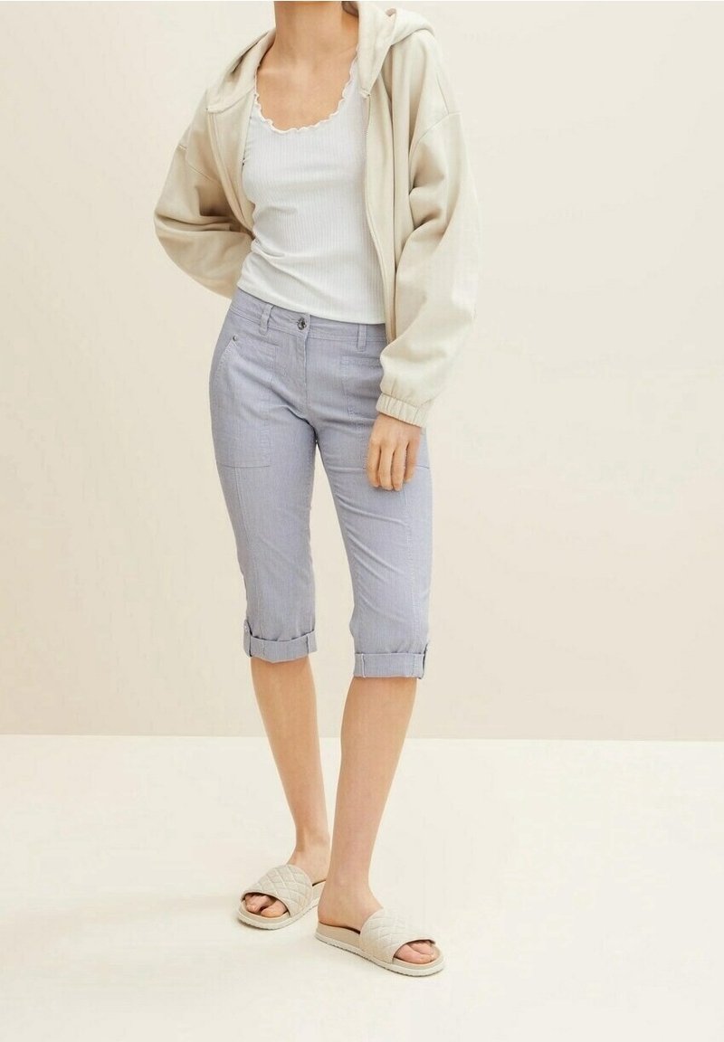 Sudadera ligera beige, camiseta sin mangas blanca de canalé y pantalones capri de cuadros azules claros hasta la rodilla. Se lleva con sandalias de slide acolchadas beige.