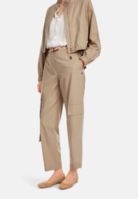 Leichte, gekürzte beige Bomberjacke, weiße Rüschene blouse, beige Cargo-Hosen mit Taschen und gewebte sandfarbene Flats.