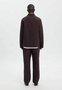 Brun stoffjakke med avslappet passform og detaljer på bakstykket, kombinert med matchende bukser; begge har en jevn tekstur og minimalistisk design.