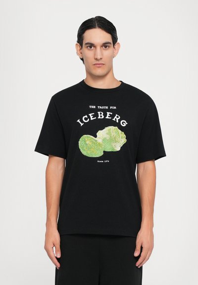 Schwarzes Baumwoll-T-Shirt mit kurzen Ärmeln, das eine Grafik von zwei Eisbergsalatköpfen und den Text "DER GESCHMACK FÜR EISBERG Seit 1974" zeigt.