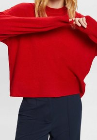 Roter Strickpullover mit hohem Kragen, überschnittenen Schultern und langen Ärmeln. Hat eine lockere Passform und gerippte Bündchen.