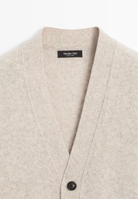 Jasnobeżowy kardigan z dekoltem w kształcie litery V, wykonany z miękkiego dzianinowego materiału, z jednym czarnym guzikiem i metką z napisem "Massimo Dutti".