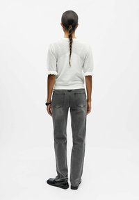 Pull blanc texturé avec des manches bouffantes, associé à un jean droit gris et des chaussures noires. Le design met en avant une coiffure tressée.