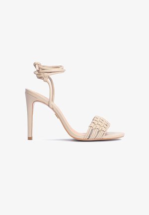 Beżowe sandały na wysokim obcasie z plecioną fakturą na pasku na palce, smukłym paskiem wokół kostki oraz spiczastym obcasem. Gładkie wykończenie.