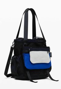 Black fabric tote bag with adjustable straps, featuring a mesh top section, a blue front pocket, and a white zippered flap accent.