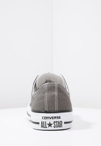 Szare płócienne trampki niskie z białymi szwami, czarną gumową podeszwą z białymi paskami oraz brandingiem "CONVERSE ALL STAR" na pięcie.