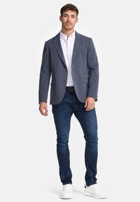 Men's grey blazer with a tailored fit, two buttons, notch lapels, and chest pocket, paired with a white shirt and dark blue jeans.