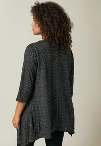 Schwarze Tunika mit einem gesprenkelten Muster, Dreiviertelärmeln und einem ausgestellten Design mit Rückenfalten für zusätzlichen Volumen und Textur.