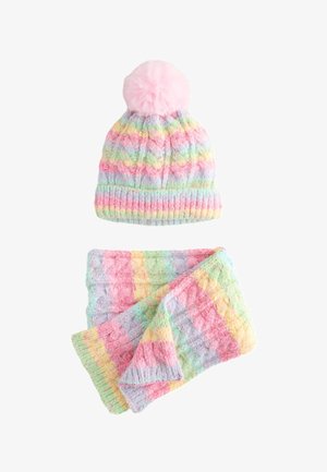 Bonnet d'hiver tricoté doux à rayures arc-en-ciel pastel avec pompon rose et écharpe assortie pliée sur fond blanc.