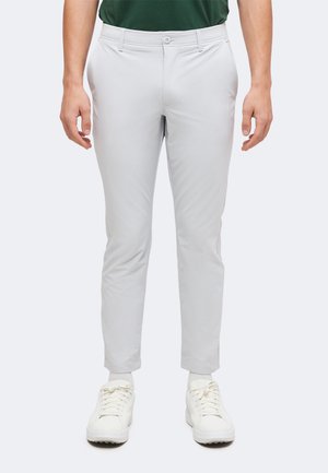 Άτομο που φοράει ανοιχτό γκρι παντελόνι slim fit, άσπρες κάλτσες, άσπρα αθλητικά παπούτσια και σκούρο πράσινο πουκάμισο, στέκεται μπροστά σε απλό φόντο.