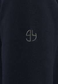 Tessuto a maglia blu navy con una sottile texture presenta un logo ricamato grigio composto da lettere intrecciate sul maniche.