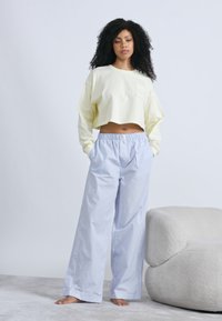 Ανοιχτόκίτρινο κοντοκομμένο τοπ με μακριά μανίκια και τσέπη μπροστά, σε συνδυασμό με ανοιχτό μπλε παντελόνι με ρίγες και φαρδιά μπατζάκια. Απαλό ύφασμα, άνετη εφαρμογή.