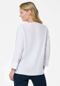 Camicia bianca con maniche a tre quarti, spacchi laterali e un fit rilassato. Tessuto morbido con un design semplice, adatta per abbigliamento casual.