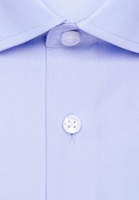 Gros plan sur le col et le devant d'une chemise bleu clair avec deux boutons blancs attachés, montrant la texture du tissu et les détails des coutures.