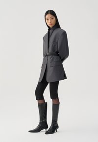 Gray oversized blazer with a high collar and patch pockets, paired with black cropped leggings and knee-high pointed toe boots.