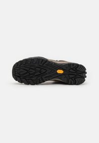 Brązowe buty trekkingowe na zewnątrz z teksturowaną czarną gumową podeszwą, wyposażone w głębokie bieżniki, z logo Vibram i solidną, wspierającą konstrukcją.