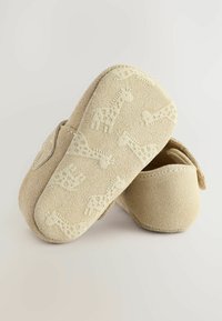 Beige mokasinisaappaat, joiden pohjissa on tekstuuriset kirahvimallit. Pehmeä materiaali, pyöreä muotoilu ja suljettu takaosa tarjoavat mukavuutta.