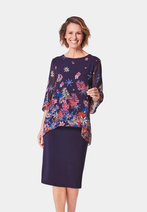Fließende navy Bluse mit floralem Muster in Pink, Rot und Blau, kombiniert mit einem dunkelblauen, taillierten Rock. Weicher, leichter Stoff, lockere Passform.