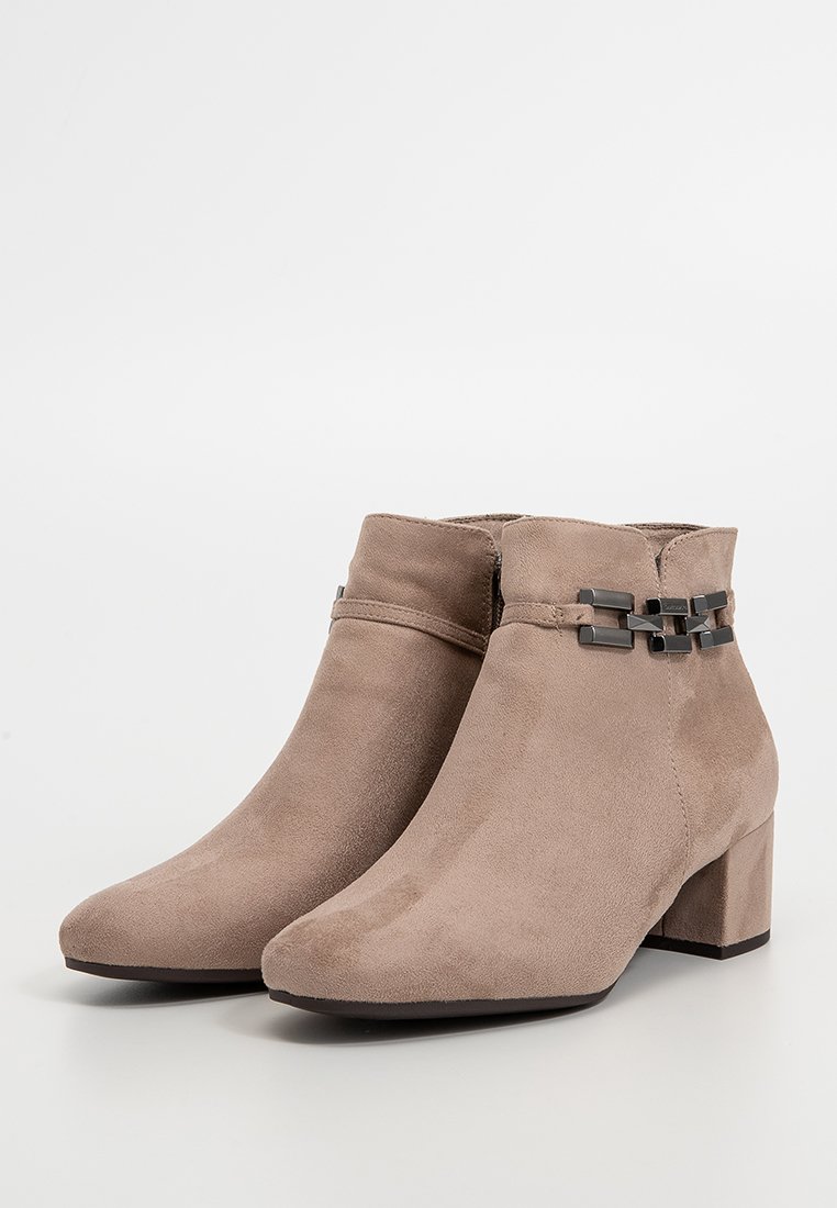 Een paar taupe suède enkellaarsjes met lage blokhakken en zwarte geometrische metalen accenten op de buitenste enkelriemen.