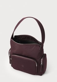 Borsa in nylon bordeaux con una singola tracolla, dotata di scomparto principale con zip e due tasche frontali con zip. Texture liscia, dettaglio del logo.
