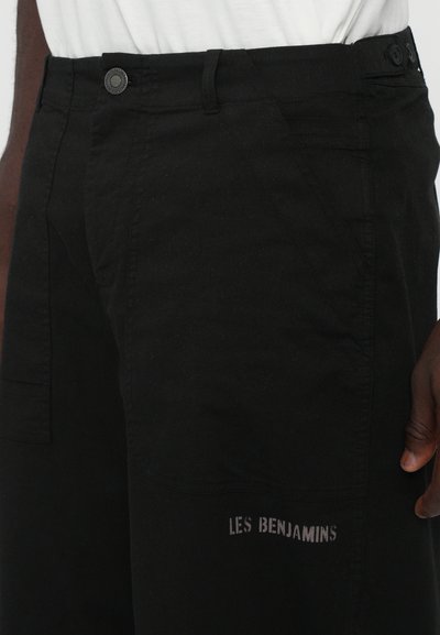 Pantalons cargo noirs en coton, présentant une coupe décontractée, des poches latérales et un logo imprimé "LES BENJAMINS" sur la cuisse.