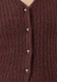 Cardigan lavorato a maglia color bordeaux con texture a coste. Presenta bottoni argentati lucidi al centro. Design a V. Materiale morbido simile alla lana.