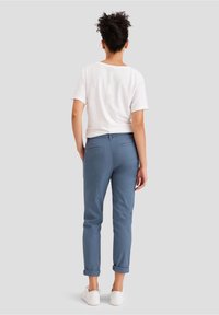 Lätt, vit kortärmad skjorta i kombination med blå chinos, uppvikta ärmkanter och vita sneakers, med en enkel, avslappnad design.