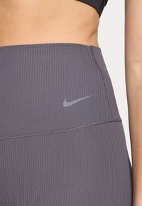 Des leggings gris côtelés avec une taille haute et des coutures subtiles. Un petit logo réfléchissant de Nike est positionné à l'avant.